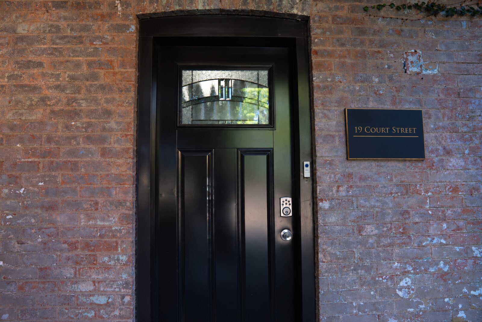 Black panelled main entrance door with leaded glass and a 19 Court Street nameplate set in exposed brick